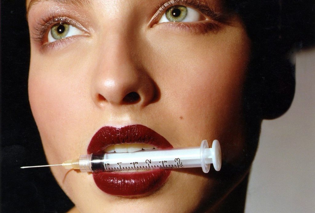 L30090102WOOAS003_003 FOR EDITORIAL USE ONLY. NOT FOR SALE IN FRANCE, ITALY AND USA. Female wearing deep berry red lipstick, holding a syringe between her teeth, unsmiling, looking up., Image: 39667433, License: Rights-managed, Restrictions: FOR EDITORIAL USE ONLY. FOR EDITORIAL USE ONLY. NOT FOR SALE IN FRANCE, ITALY AND USA., Model Release: no, Credit line: Profimedia, TEMP Camerapress