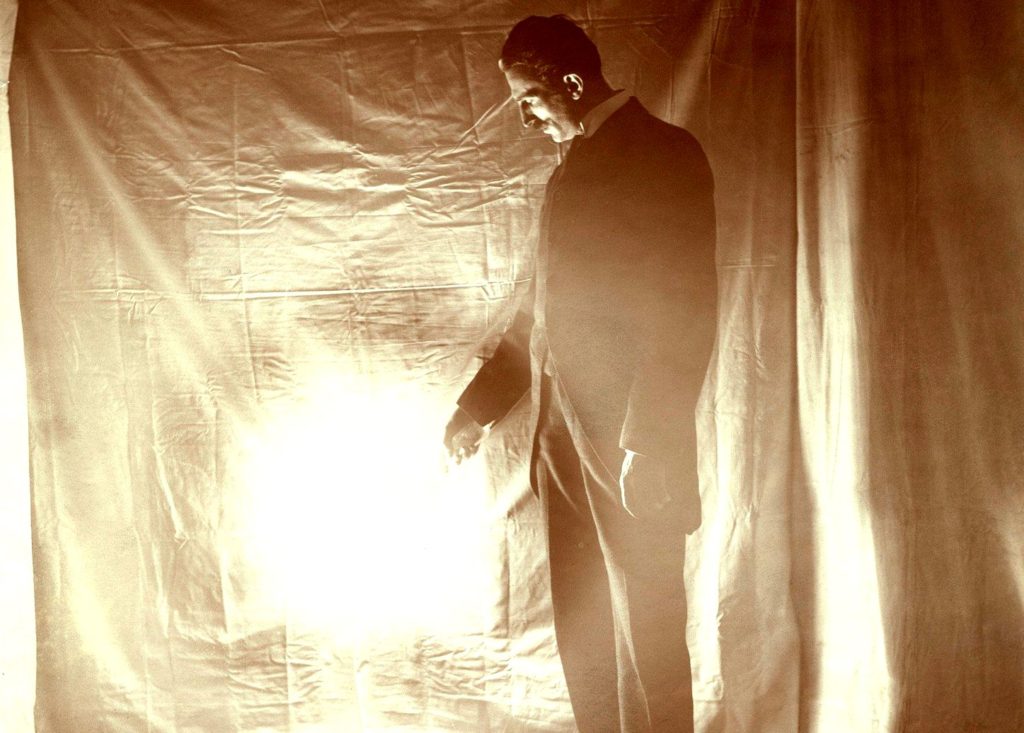 Nikola Tesla (1856-1943), Serb-US physicist and electrical engineer, holding the gas-filled phosphor-coated 'wireless light bulb' that he had developed in the 1890s. Tesla was educated at Graz and Prague, but in 1884 he emigrated to the USA. For a while he worked with Edison, but soon left to work on his own. He developed the alternating current (a.c.) induction motor, and helped advance a.c. power generation and transmission. He also worked on high-frequency a.c. currents, inventing the Tesla Coil, a transformer in which the primary and secondary coils are in resonance. He used it to create electric sparks 40 metres long, and in 1899 lit 200 electric lamps without wires. The SI unit of magnetic flux density is named for him. Photographed in Tesla's laboratory at 46-48 East Houston Street, New York, USA., Image: 324244397, License: Rights-managed, Restrictions: Editorial use only, Model Release: no, Credit line: Profimedia, Sciencephoto RM
