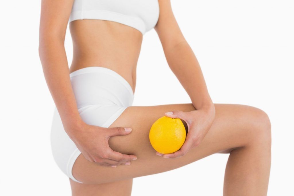 Slender female body holding orange and squeezing her thigh