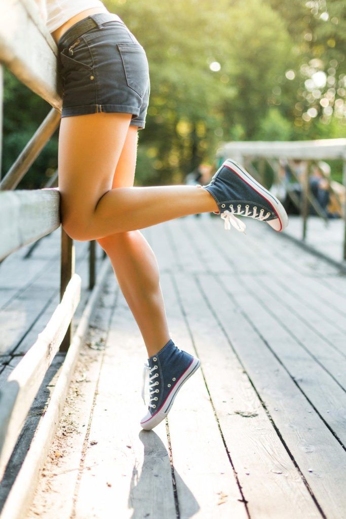 Young woman with beautiful sporty legs leaning on a wooden bridge railing in jeans sneakers