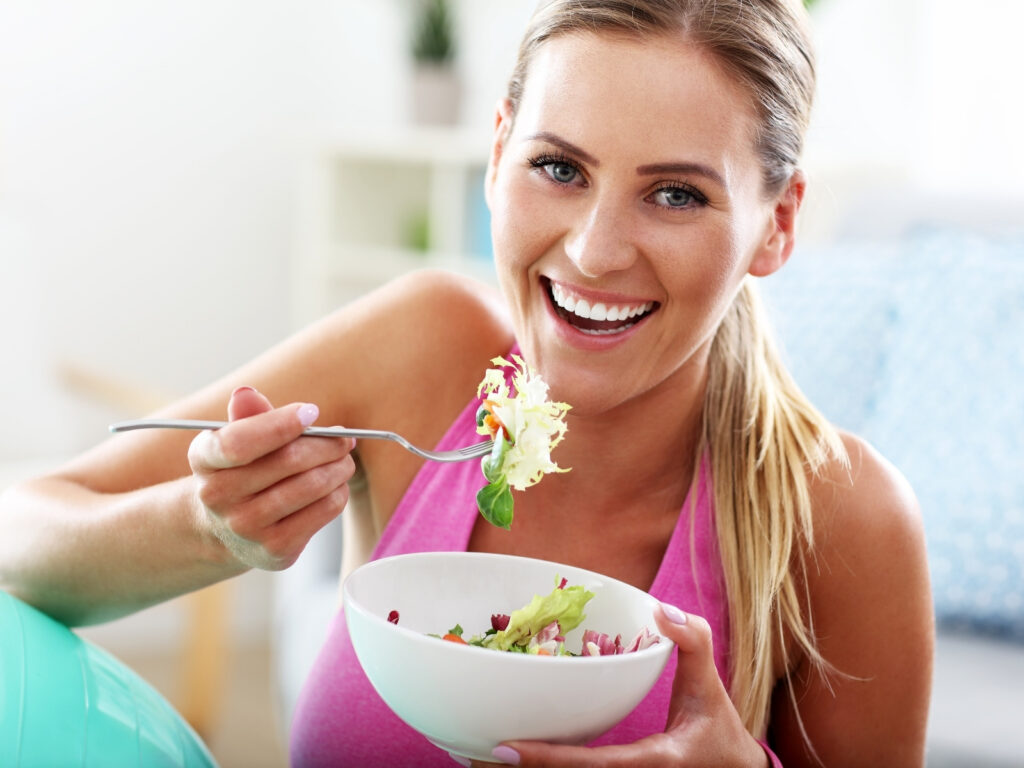 Nasmijana žena nakon treninga jede svježu salatu kao lagan i nutritivno bogat obrok