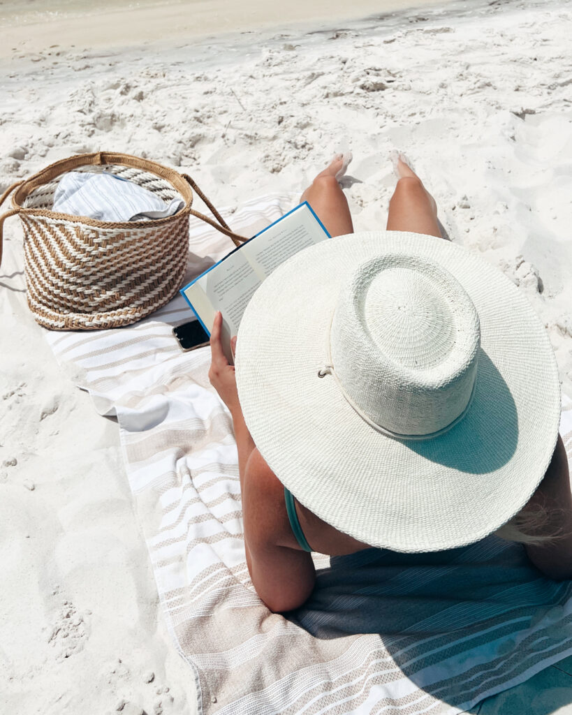 Žena čita knjigu na plaži sa šeširom kao zaštitom od sunca