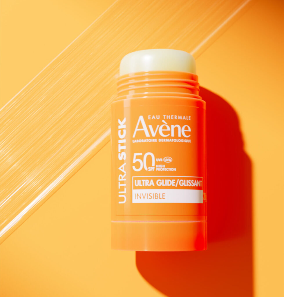 Krupni kadar Avène Ultra Stick SPF50 na narančastoj pozadini s efektom sunčevih zraka
