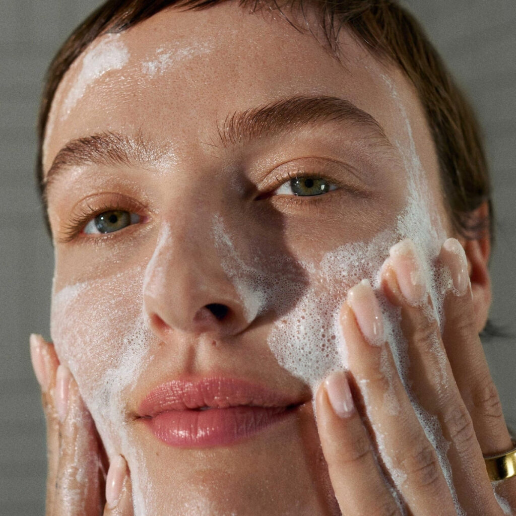 Žena nanosi kremastu pjenu Dermalogica Daily Microfolianta na lice kružnim pokretima