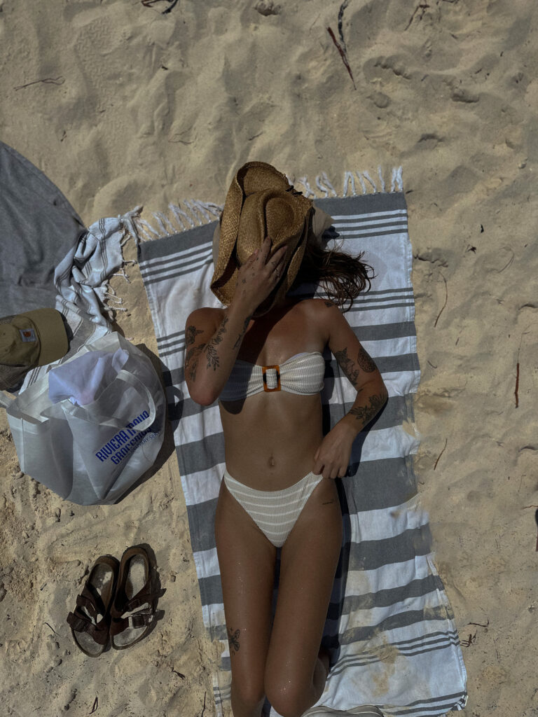 Žena prekrivena slamnatim šeširom uz torbu za plažu leži na ručniku