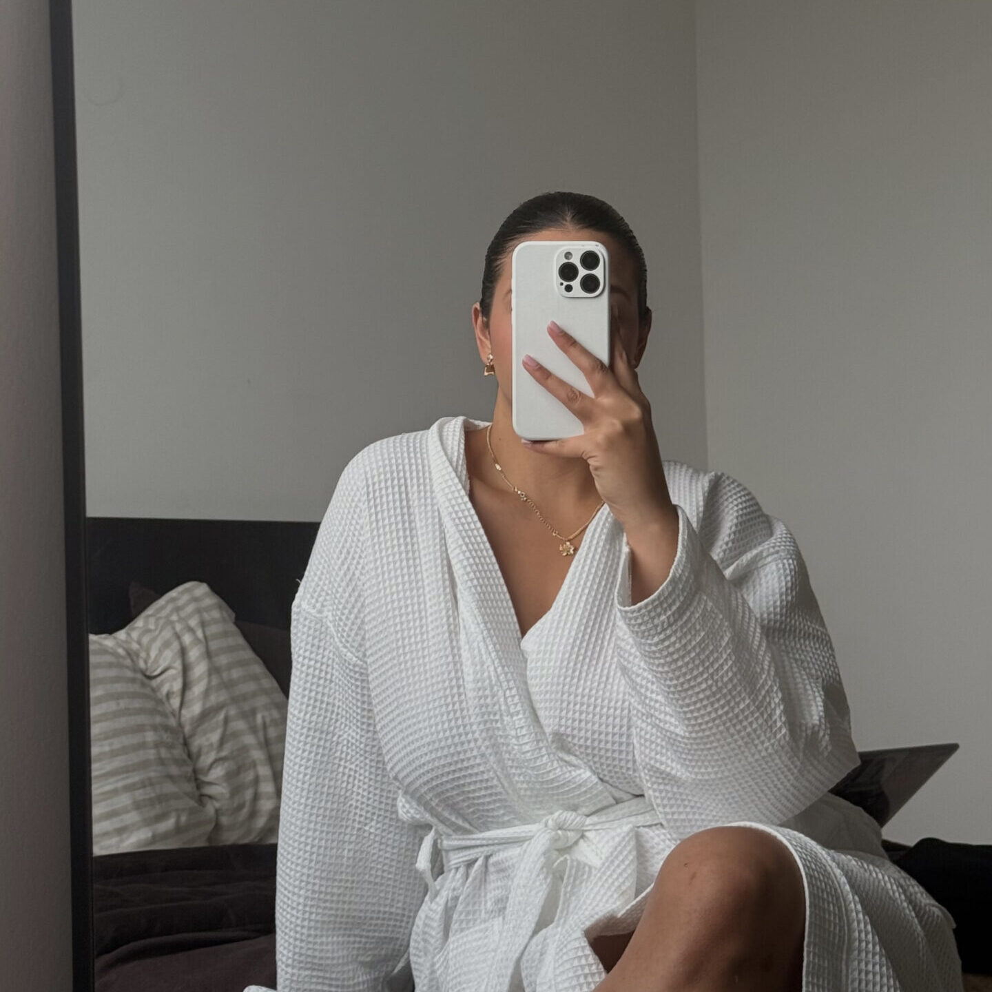 Žena u bijelom ogrtaču snima fotografiju u ogledalu tijekom beauty rutine