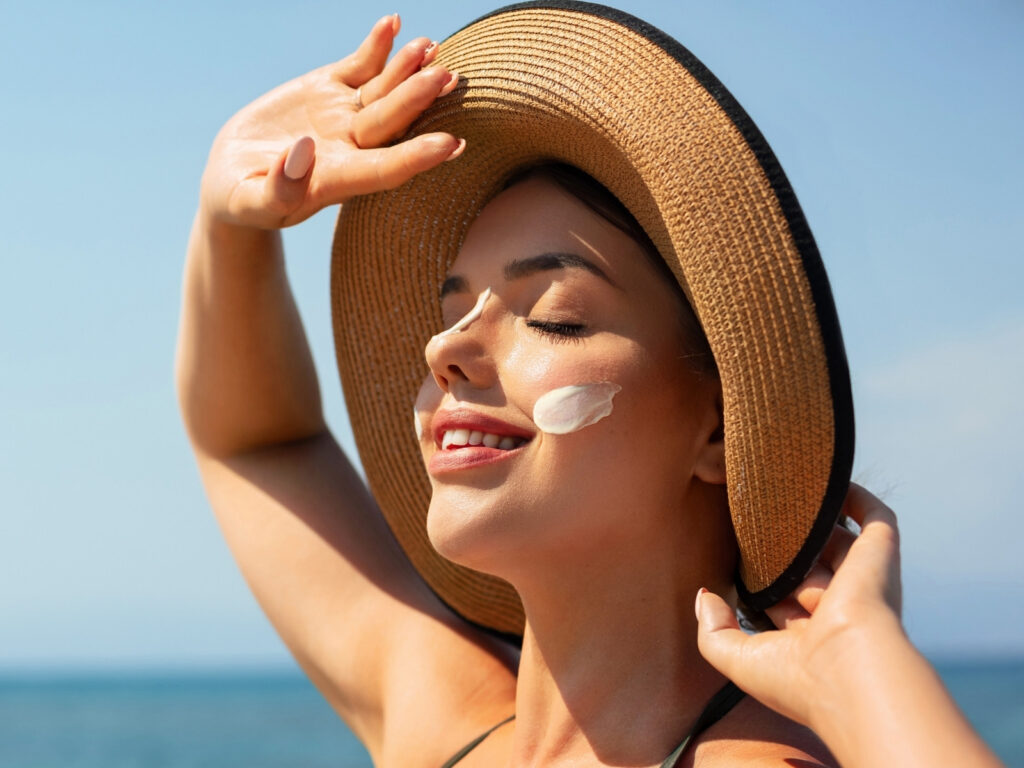 Žena sa slamnatim šeširom i kremom za sunčanje na licu uživa na plaži