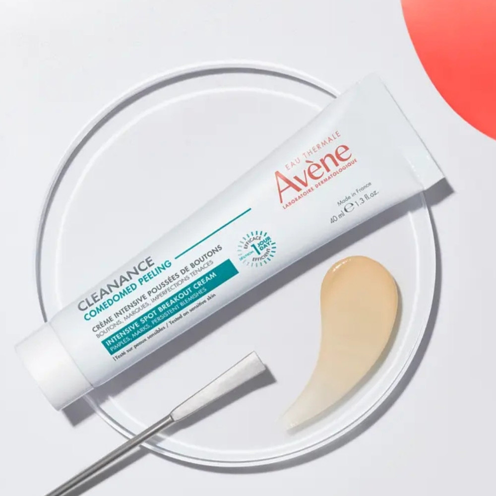 Avène Cleanance Comedomed Piling Intenzivna krema prikazana uz teksturu proizvoda na laboratorijskoj podlozi.