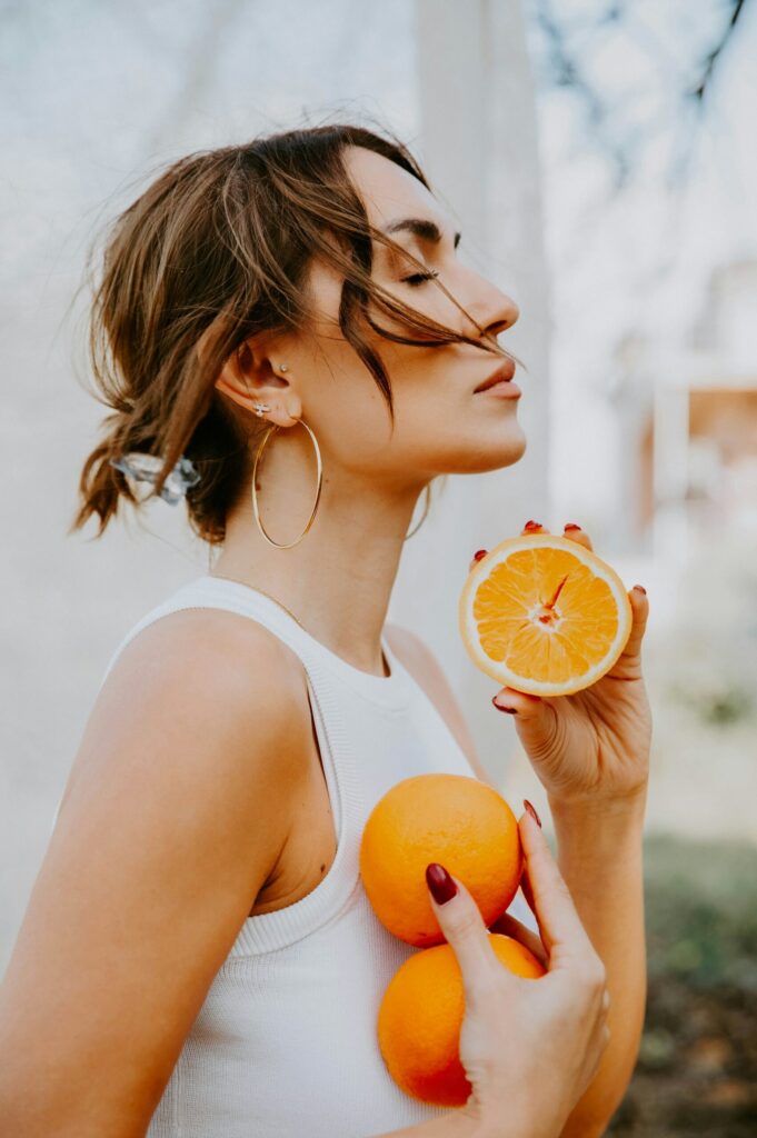 Žena drži naranče i polovicu naranče, izvor vitamina C važnog za zdravlje kose
